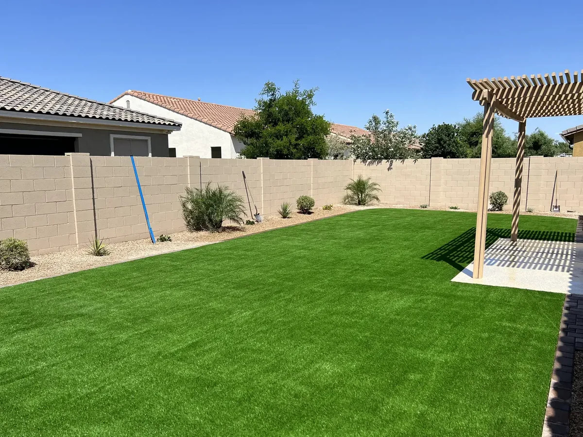 Pergola on a concrete pad beside a new artificial turf lawn with block walls and gravel planting beds