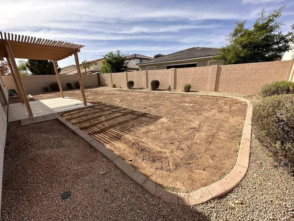 Backyard graded under a pergola before the turf and paver install