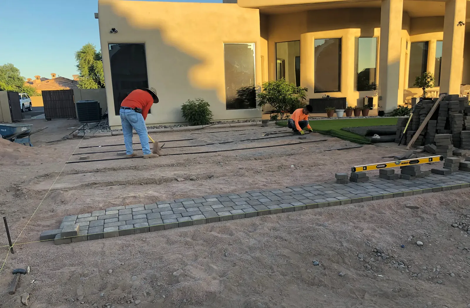 Paver patio and sod installation in progress behind a yellow stucco home