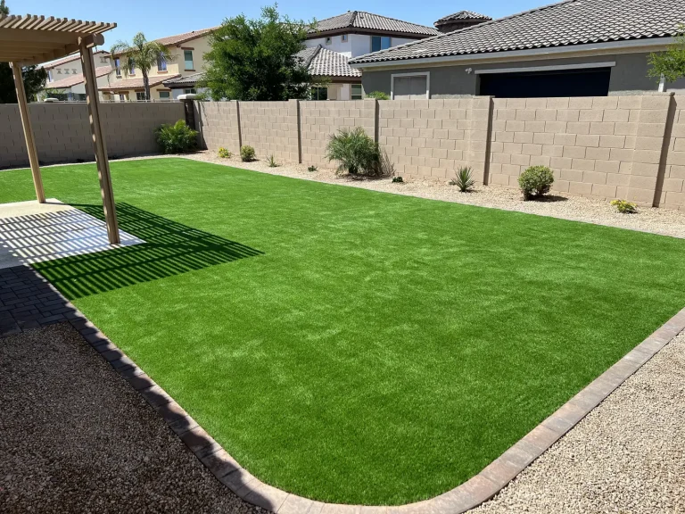 Backyard artificial turf lawn with a shrub border and pergola
