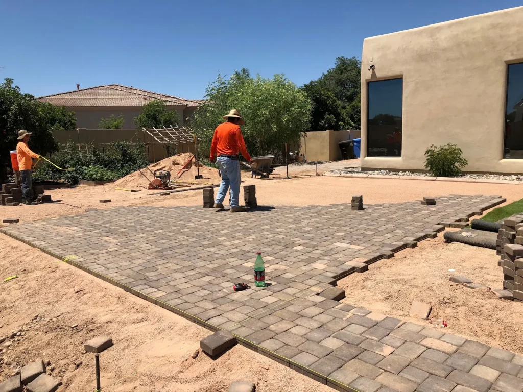 Crew laying a paver patio behind a stucco home