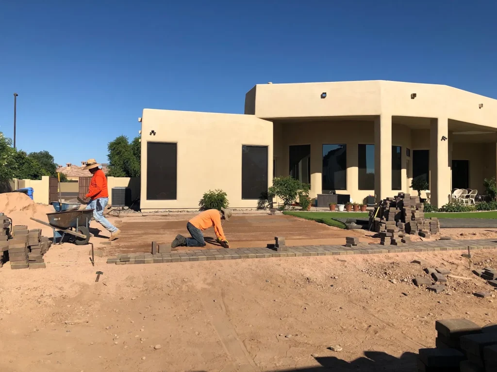 Crew laying pavers on a graded base behind a new home