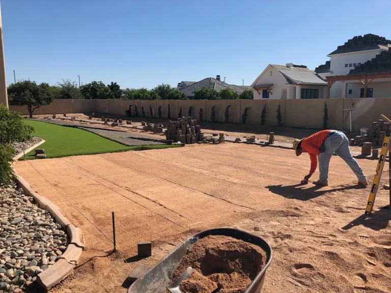 Crew leveling the base for a paver patio next to new artificial turf