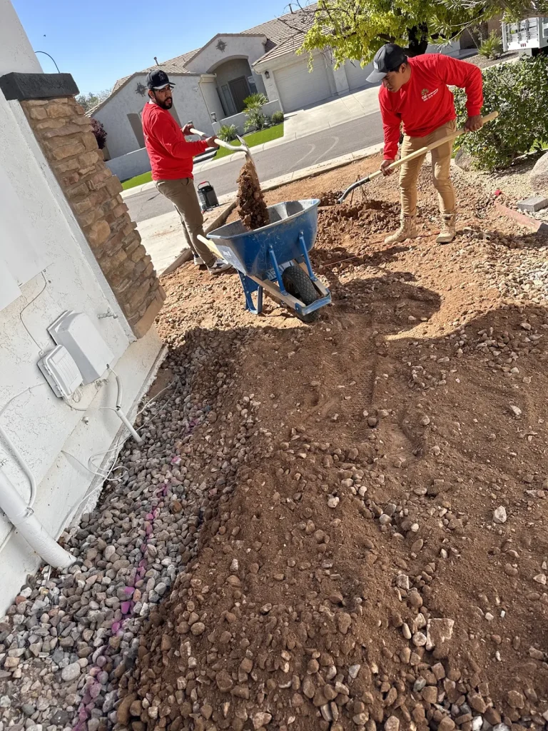 Crew members shoveling soil into a wheelbarrow in a front yard planting bed
