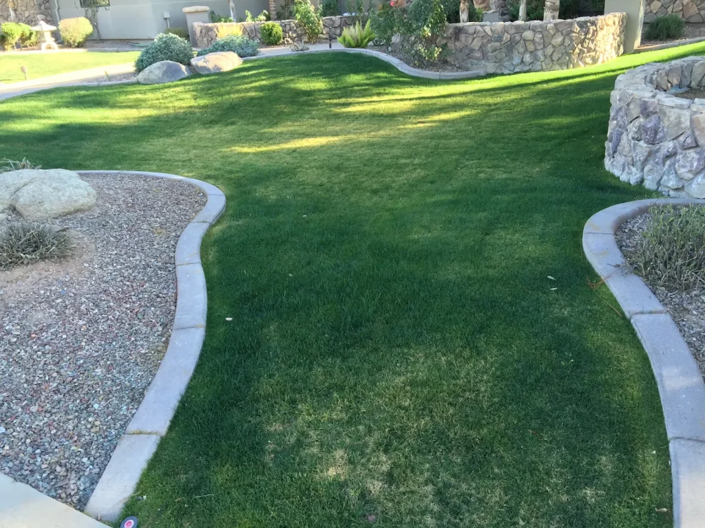 Curved grass lawn edged with concrete curbing, gravel beds and a stone wall