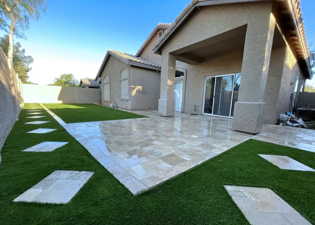 Travertine paver patio with artificial turf inlay strips in a finished backyard