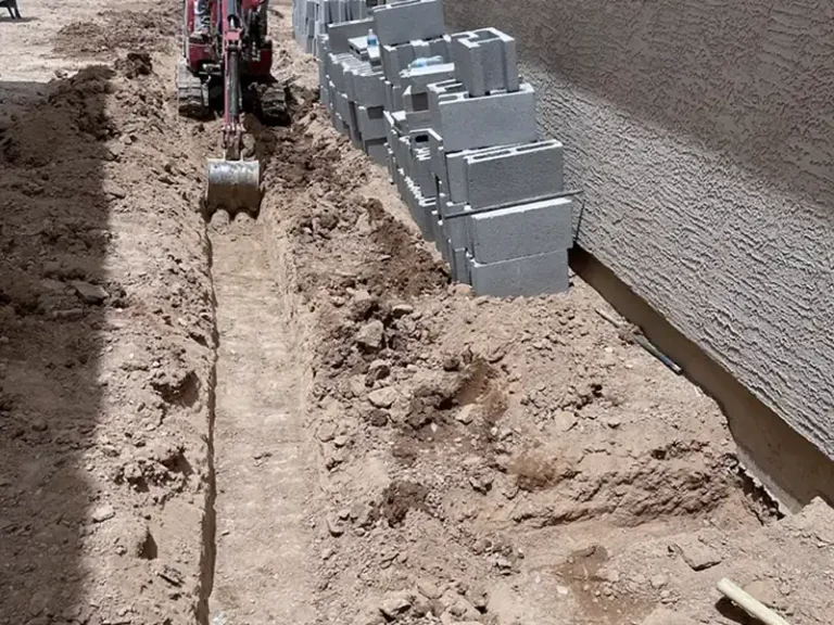 Mini skid steer trenching a side yard for irrigation lines and retaining wall block