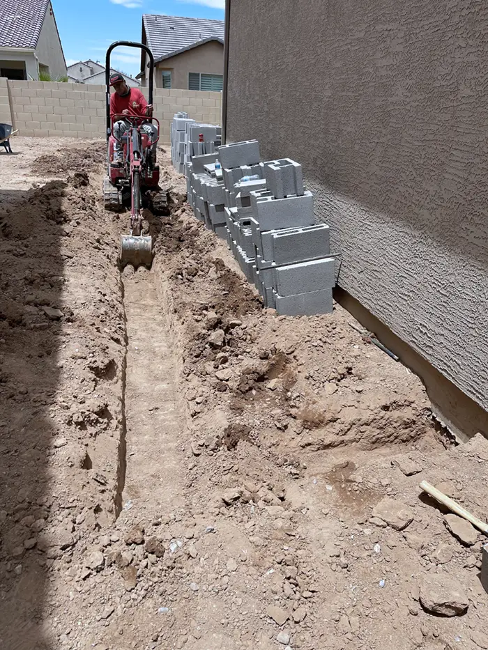 Mini skid steer trenching a side yard for irrigation lines and retaining wall block