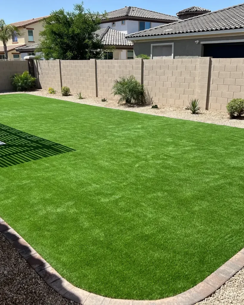 Backyard artificial turf lawn with a shrub border and pergola